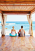 Couple meditating together in cabana overlooking ocean