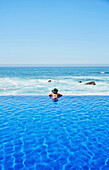Mixed race woman relaxing in infinity pool