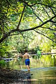 Toddler boy searches for pollywogs with net at creek in Bidwell Park, Chico, California.