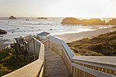 Evening light shines on a long wooden staircase leads down to Bandon Bay on the Oregon Coast.