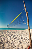 Two rough sticks hold up a beach volleyball net set up beside the ocean on Playa La Jaula beach, Cayo Coco, Cuba.