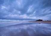 Storm clouds reflect on the deserted beach beside Bamburgh Castle in winter, Northumberland, England, United Kingdom, Europe