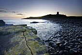 View across the Rumble Churn at dawn towards the ruins of Dunstanburgh Castle, Embleton Bay, near Alnwick, Northumberland, England, United Kingdom, Europe