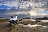 View across Aln Estuary at low tide showing boat and distanyt fields covered in snow and sun breaking through winter sky, Northumberland, England, Uninted Kingdom, Europe