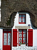Exterior of a thatched cottage with red door and shutters in La Grande Briere, Ile de Fedrun, Pays de la Loire, France, Europe