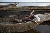 A boy relaxes in a dugout canoe on the Congo River, Yangambi, Democratic Republic of Congo, Africa