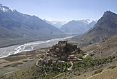 Backlit view of Kee Gompa monastery complex from above, with Spiti valley and snowy mountains beyond, Spiti, Himachal Pradesh, India, Asia