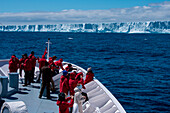 Passengers on bow of expedition cruise ship MS Hanseatic (Hapag-Lloyd Cruises) with giant iceberg in distance, near Shag Rocks, South Atlantic Ocean between Falkland Islands and South Georgia Island, Antarctica