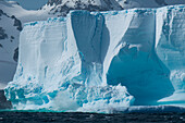 Waves crash against giant iceberg with mountains behind, near Livingstone Island, South Orkney Islands, Antarctica