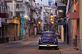 View along quiet street at dawn showing old American car and street lights still on, Havana Centro, Havana, Cuba, West Indies, Caribbean, Central America