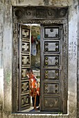 Young boy curiously looking through an old antique door, Moroni, Grand Comore, Comoros, Indian Ocean, Africa
