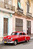 Restrored red American car pakred outside faded Colonial buildings, Havana, Cuba, West Indies, Central America