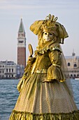 Masked carnival character in costume, the lagoon beyond, Campo San Giorgio, Island of San Giorgio Maggiore, Venice, Veneto, Italy, Europe