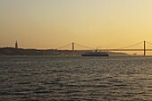 A cruise liner turns into the sunset, on the River Tagus under the 25 April Bridge and Christus Rei statue, Lisbon, Portugal, Europe
