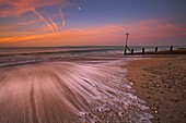 The moon still glows above the surging tide at sunrise on Hayling Island, Hampshire, England, United Kingdom, Europe