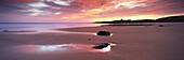 View along Embleton Bay at sunrise, with silhouette of Dunstanburgh Castle in the distance, near Alwick, Northumberland, England, United Kingdom, Europe