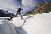 Climber jumping across a crevase stream on Mer de Glace glacier, Mont Blanc range, Chamonix, French Alps, France, Europe