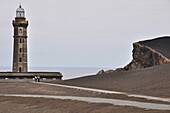 Zwei junge Frauen wandern am Leuchtturm am Strand mit Vulkan Vulcao dos Capelinhos, Farol dos Capelinhos, Ponta dos Capelinhos, Insel Faial, Azoren, Portugal, Europa, Atlantik