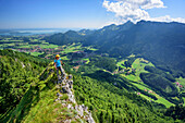Woman hiking walking on small ridge, lake Chiemsee and Kampenwand in background, Zellerhorn, Chiemgau Alps, Upper Bavaria, Bavaria, Germany