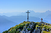 Frau beim Wandern geht auf Gipfelkreuz des Zennokopf zu, Watzmann im Hintergrund, Zennokopf, Chiemgauer Alpen, Oberbayern, Bayern, Deutschland