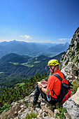 Man ascending fixed rope route and writing into summit book, Watzmann in background, Hochthronklettersteig, fixed rope route Hochthron, Untersberg, Berchtesgadener Hochthron, Berchtesgaden Alps, Upper Bavaria, Bavaria, Germany