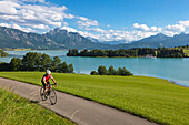 Biker at Forggensee, view to Neuschwanstein castle, Saeuling and Tannheimer Berge, Allgaeu, Bavaria, Germany