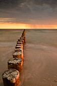 Buhnen am Strand an der Ostsee mit Gewitterhimmel zu Sonnenuntergang, Zingst, Nationalpark Vorpommersche Boddenlandschaft, Halbinsel Zingst Darß Fischland, Mecklenburg-Vorpommern, Deutschland