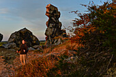 Young woman is hiking along rock formation Devil´s Wall (Teufelsmauer) at sunset, Neinstedt, Thale, Harz Foreland, Harz Mountains, Saxony-Anhalt, Germany