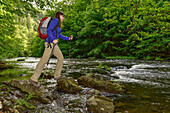 Young woman is hiking over stones at river Bode at Bode Valley (Bodetal) on the hiking trail Harzer Hexen Stieg from Thale to Treseburg, spring, Harz Foreland, Harz Mountains, Saxony-Anhalt, Germany