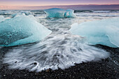 Glacial ice from Breiðamerkurjökull sits on the beach  of the coast at Breiðamerkursandur, Iceland, also known as the Jokulsarlon.