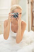 Bride photographing with vintage camera on bed
