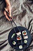 Hands of woman reaching for platter of sushi on bed
