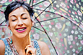 Older Caucasian woman with eyes closed holding umbrella