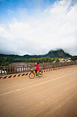 A young woman cycles in Northern Laos town of Nong Khiaw, along the Ou River, Nong Khiaw, Laos