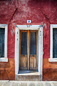 A close view of a door on a rustic red house, Burano, Venice, Italy