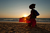 Silhouette of a woman selling Indian cloth on the beach at dusk, Candolim, Goa, India