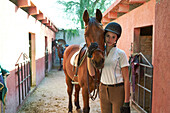 Teenage girl leading horse in stable on ranch