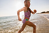 Caucasian girl running in ocean waves on beach