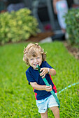 Caucasian baby boy playing with hose in backyard