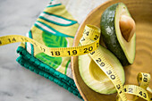 Close up of halved avocado, measuring tape and napkin on plate