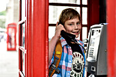 Boy (11) inside a typical British, red phone box with telephone in his hand, London, Great Britain