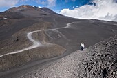 Large ash field with car tracks at the foot of the Etna in about 3000m altitude. Woman walking through the ash field, Sicilian, Italy