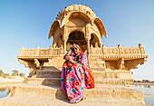 Indian woman in traditional clothes sitting near monument, Jaisalmer, Rajasthan, India
