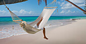 Caucasian woman laying in hammock on tropical beach
