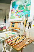 Paintbrushes, palette and easel with painting in studio