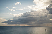Sailboats under clouds on ocean