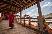 A monk (lama) of Punakha Dzong crosses the wooden bridge over the river that provides access to the ancient monastery, Bhutan, Asia