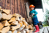 Junge, 4 Jahre, mit Spielzeug Motorsäge vor Alpinhütte, Feuerholz vor Alpenhütte, Maria Alm, Berchtesgadener Alpen, Österreich, Europa