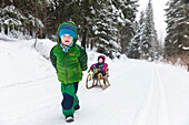 Little boy pulling his sister on a sled through a winter forest, MR, Holzhau, Saxony, Germany