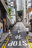 Stop, sign, narrow street in Hong Kong, asphalt, writing, symbols, pedestrians, tree between the high-rise apartments, blocks of flats, Hong Kong, China, Asia